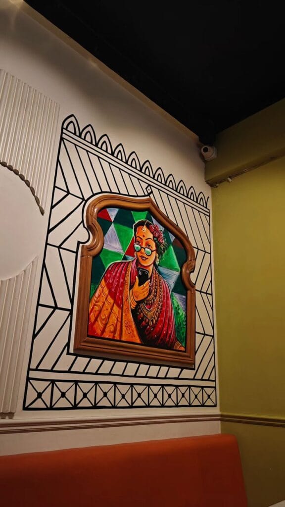 A wall-mounted framed painting of a woman in traditional Indian attire and glasses, holding a smartphone.