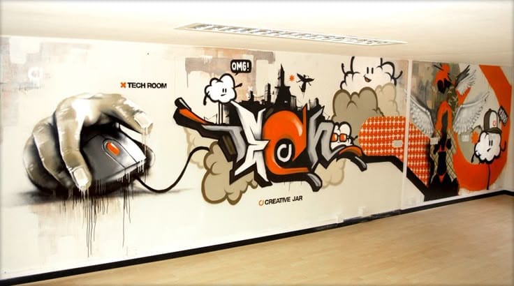 A wide graffiti mural on a white office wall featuring a large hand using a computer mouse, stylized "TECH" lettering in orange and white, and various cartoon characters and urban elements.