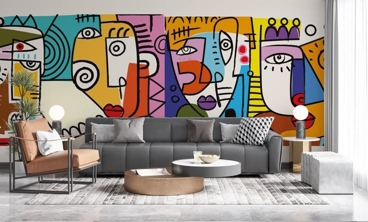 A large, colorful wall mural behind a grey sofa featuring bold, childlike abstract faces with thick black outlines and bright primary colors.