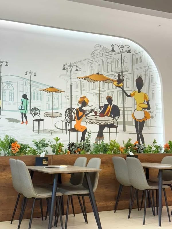 A cafe interior featuring a large wall mural with black and yellow silhouettes of a couple dining and a waitress serving, set against a sketch of historic city buildings.