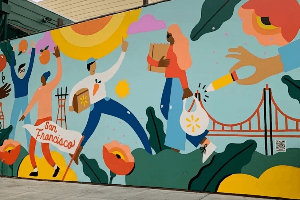 A wide mural on a city wall featuring flat-style illustrations of people carrying groceries and a "San Francisco" banner against a backdrop of the Golden Gate Bridge and poppies