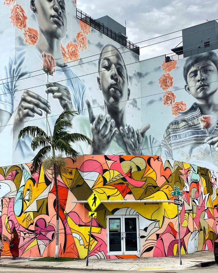 A large-scale building mural featuring hyper-realistic grayscale portraits with floating roses above a vibrant, abstract graffiti base.