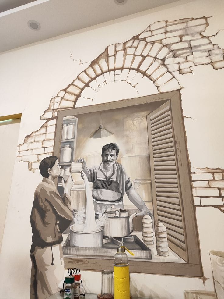 A large-scale, sepia-toned wall mural depicting a traditional tea vendor (chaiwala) pouring steaming milk from a height into a pot. The artwork is framed by a painted 3D effect of a weathered brick archway and wooden shutters, creating a "window" into a rustic kitchen scene. A young man stands to the left, waiting for his tea. The style uses shades of brown and cream to evoke a nostalgic, vintage feel.