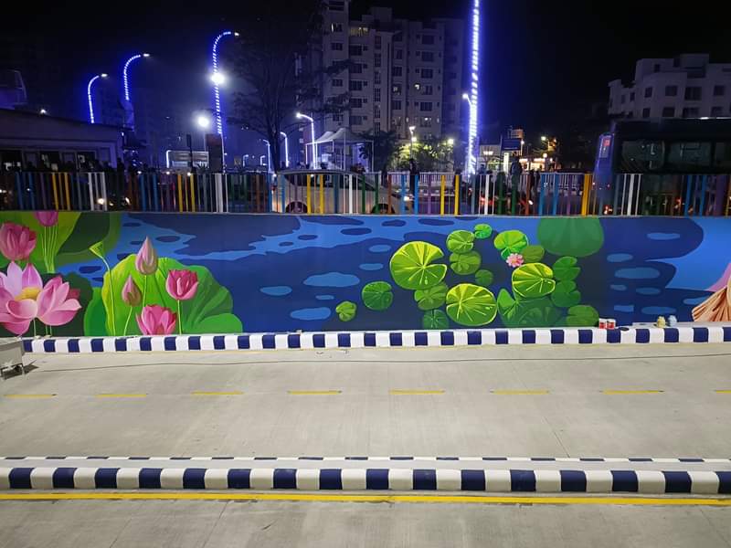 Colorful lotus pond mural painted on an outdoor boundary wall with floating lily pads and floral artwork at night.