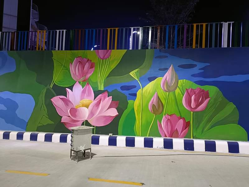 Colorful lotus pond mural painted on an outdoor boundary wall with floating lily pads and floral artwork at night.