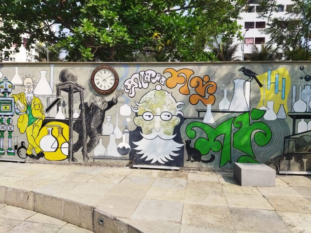 Hand-painted science-inspired street art mural featuring laboratory elements, abstract illustrations, and artistic Bengali typography on an outdoor wall.