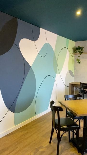 Abstract wall painting with soft blue, green, and beige organic shapes designed for modern café interiors.